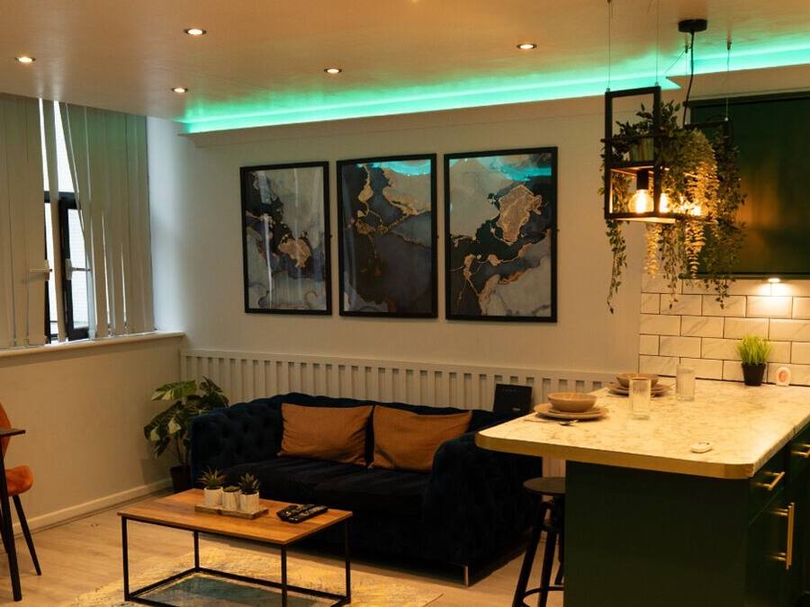Una sala moderna con un sofá azul oscuro, una mesa de centro de madera y una cocina con gabinetes verdes y una encimera blanca.