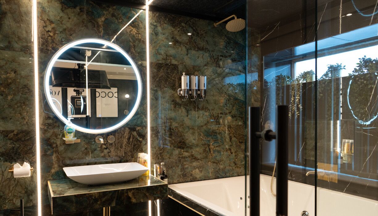 Un baño moderno con un espejo grande, un lavamanos blanco y una zona de ducha con paredes de vidrio.