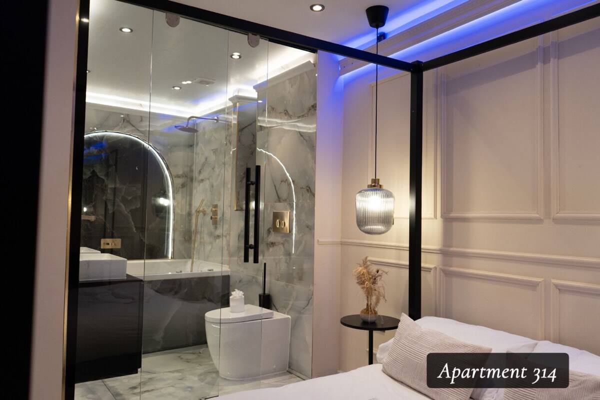 A modern bedroom with a large bed, a glass-enclosed bathroom, and a pendant light.