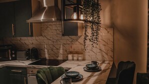 A modern kitchen with a marble countertop, green chairs, and a hanging plant. - The Opulence (Bradford)