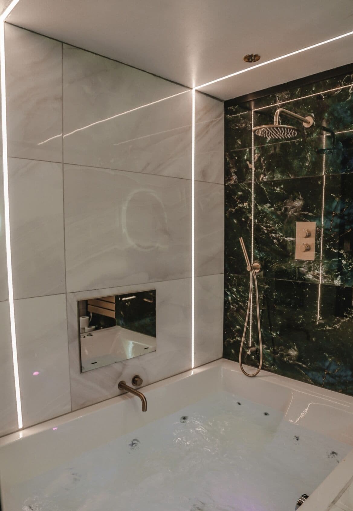 A modern bathroom with a large bathtub, a handheld showerhead, and a wall-mounted mirror.