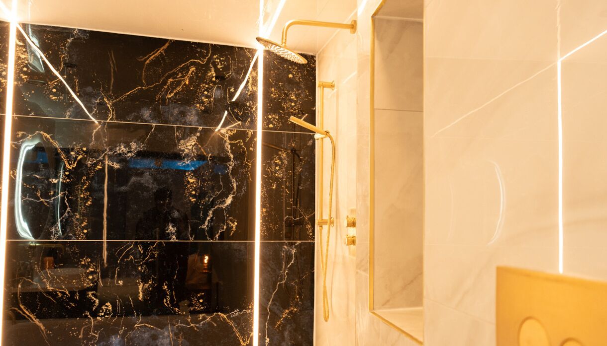 A modern bathroom with a black marble shower enclosure and gold fixtures.