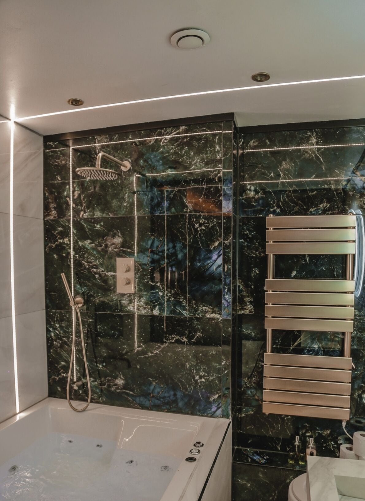 Ein modernes Badezimmer mit einer Duschwand aus Marmor, einer integrierten Badewanne und einem an der Wand befestigten Handtuchhalter.