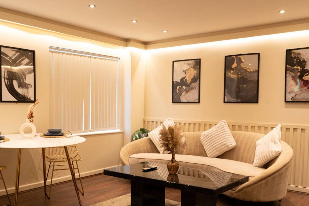 A modern living room with a round dining table, two chairs, a sofa, and three framed artworks on the wall.