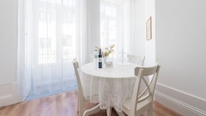 Une table ronde recouverte d’une nappe en dentelle, deux chaises, une bouteille d’eau, un vase de fleurs et un panneau d’accueil.