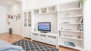 Un salon moderne avec un téléviseur à écran plat, des étagères blanches et un tapis noir à motifs.