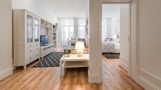 Une pièce moderne et bien éclairée, dotée d’un plancher en bois, d’un meuble blanc aux portes vitrées, d’un téléviseur et d’un coin repas avec une table et des chaises.