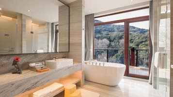 A modern bathroom with a large bathtub, two sinks, a vanity with a mirror, and a view of a mountainous landscape.
