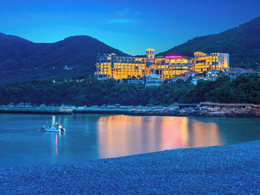 Un gran hotel con varios pisos y balcones, ubicado en una colina con vistas a una masa de agua tranquila.