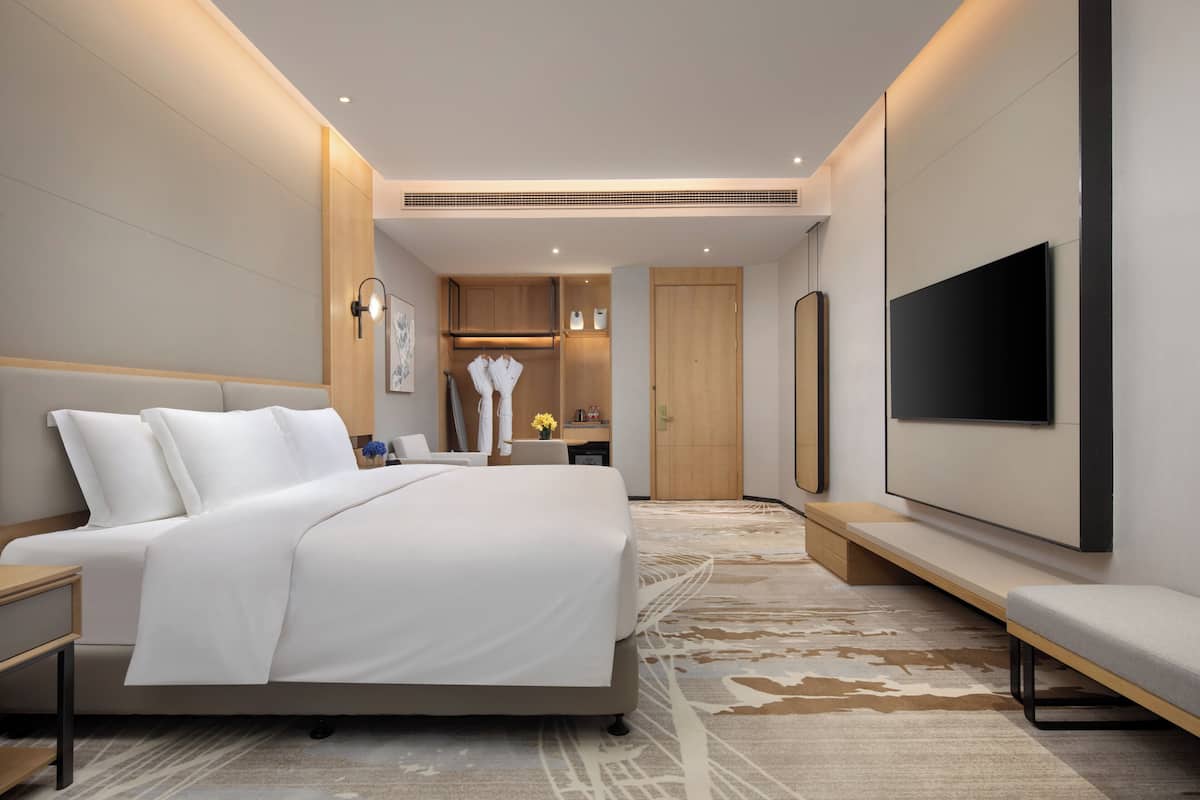 A modern hotel room with a large bed, a TV mounted on the wall, and a small seating area.