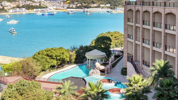 Un hotel con zona de piscina, un pabellón y vistas al mar con barcos.