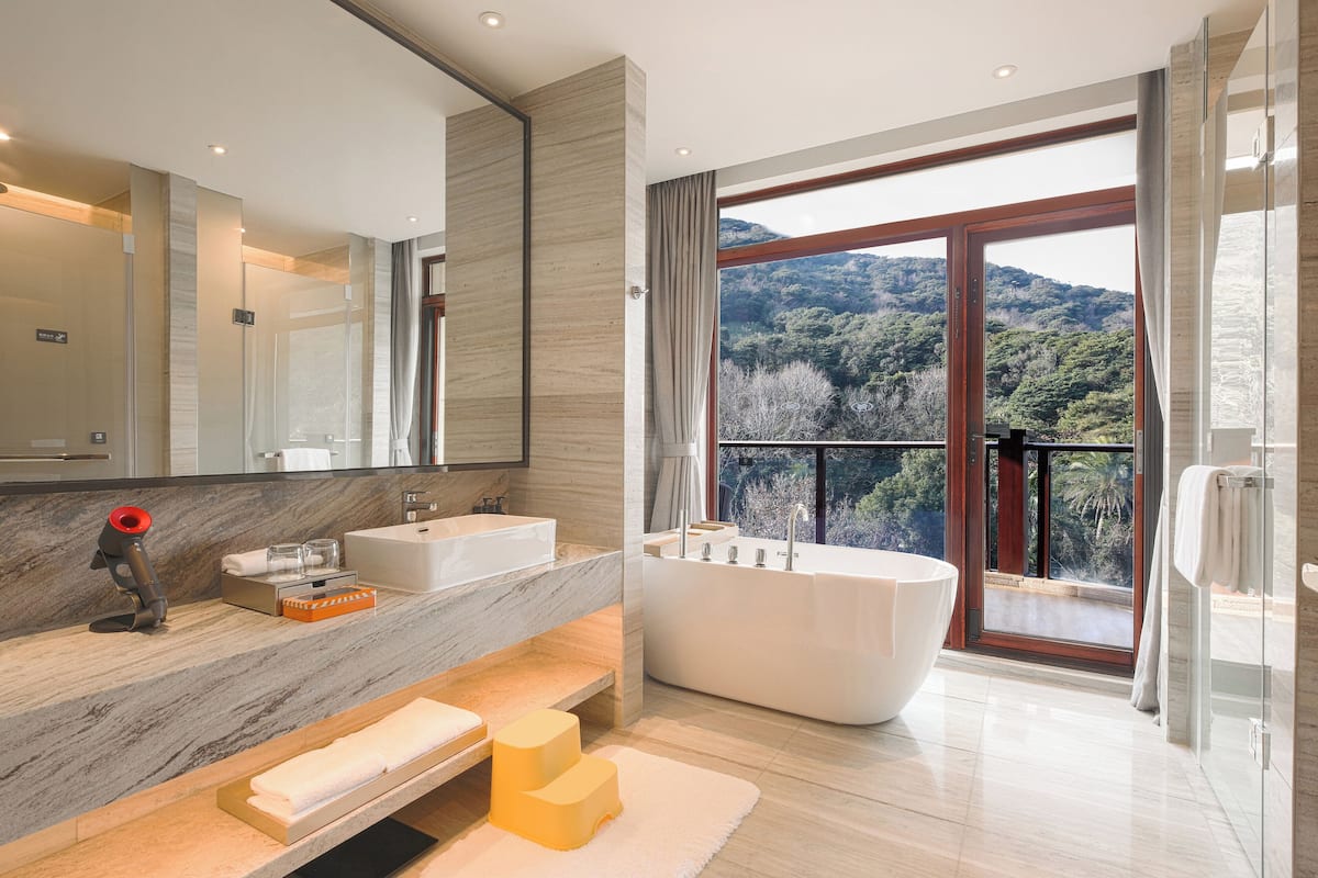 A modern bathroom with a large bathtub, two sinks, a vanity with a mirror, and a view of a mountainous landscape.