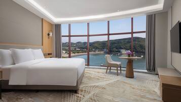 Ein Hotelzimmer mit einem großen Bett, einer Sitzecke und Blick auf ein Gewässer und Hügel.