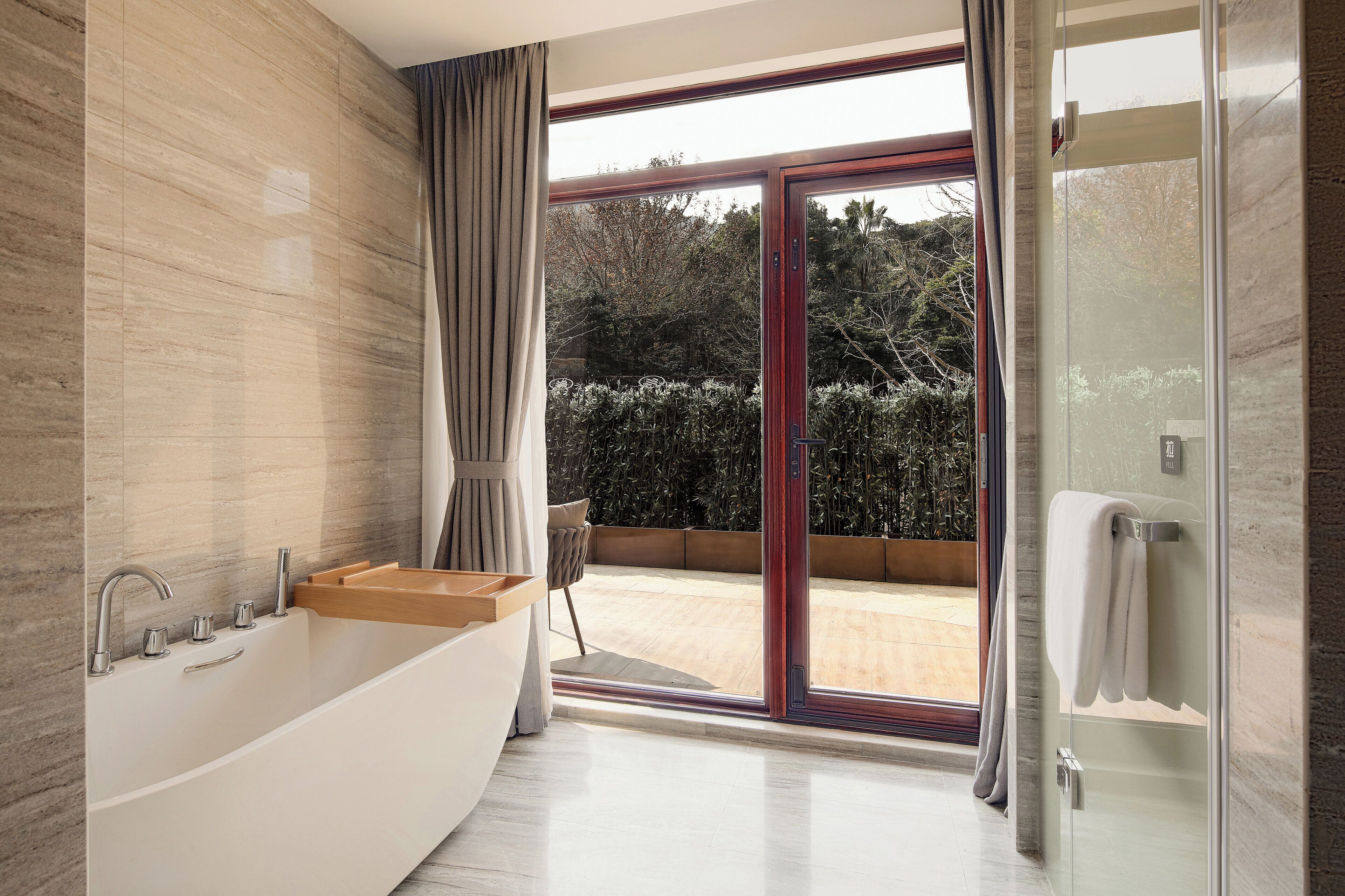 Une salle de bain moderne avec une baignoire sur pieds, une douche à parois de verre et une vue sur un espace extérieur aménagé, visible à travers de grandes portes coulissantes en verre.