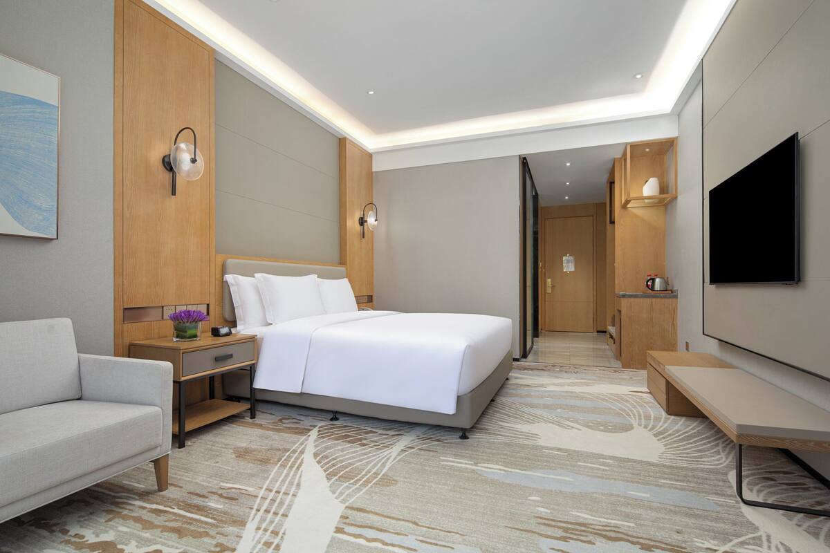 A modern hotel room with a large bed, a sofa, a TV, and a wooden cabinet.