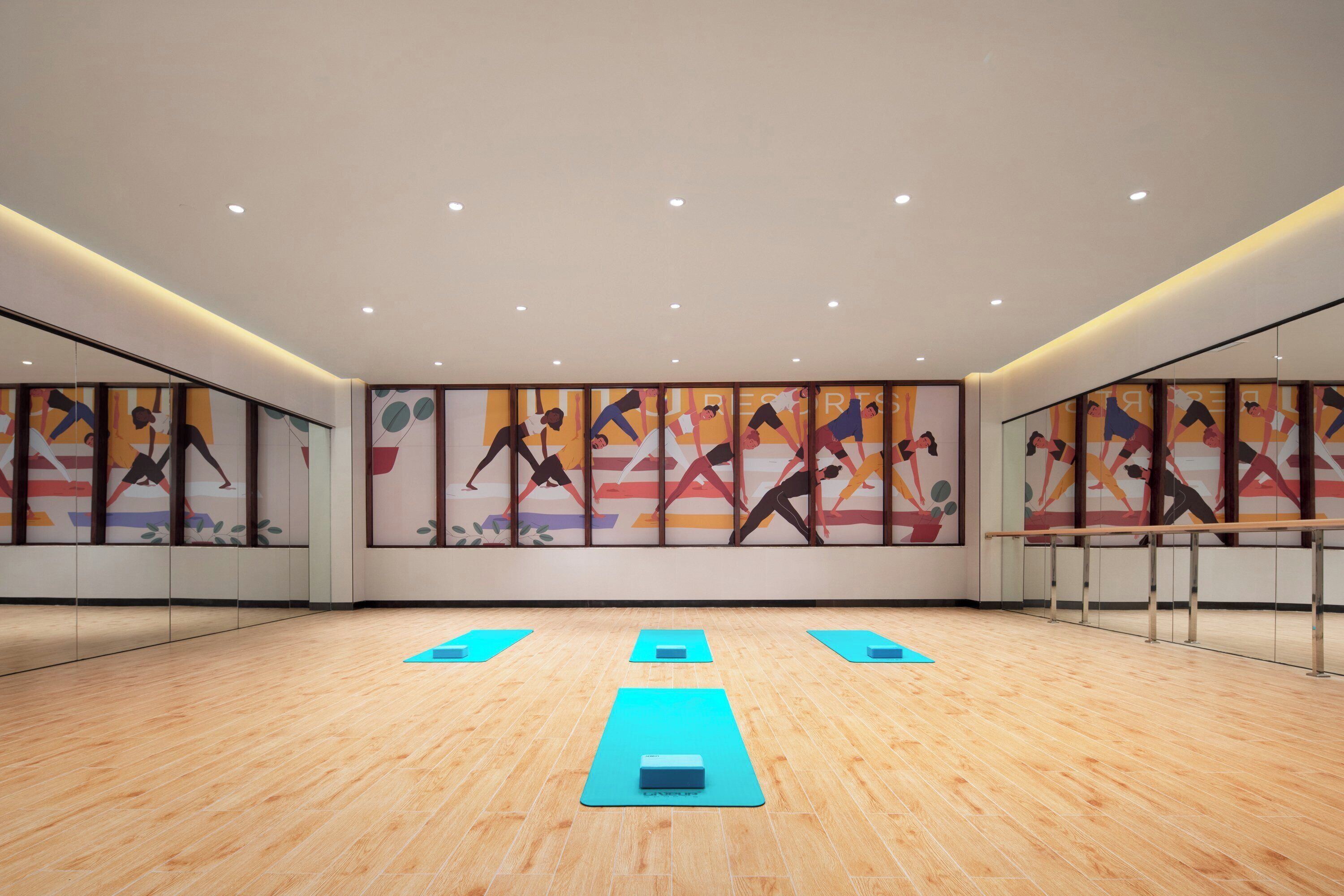 Amplia habitación con piso de madera, paredes espejadas y colchonetas de yoga dispuestas para ejercitarse.