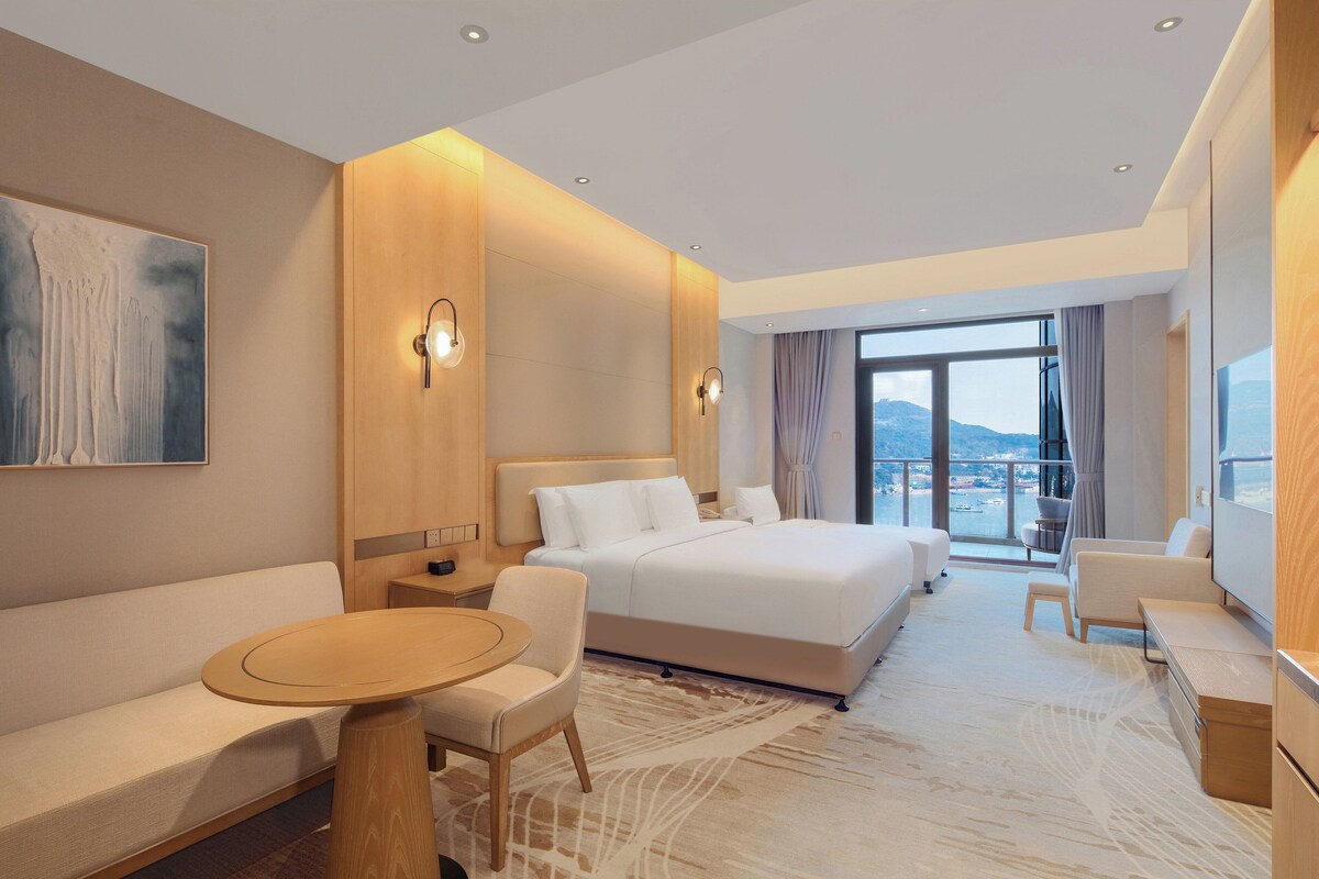 Une chambre d’hôtel moderne dotée d’un grand lit, d’un canapé, d’une table à manger et offrant une vue sur la ville.