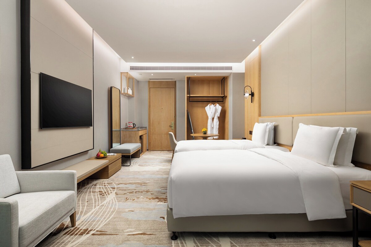 A modern hotel room with a large bed, a flat-screen TV, a seating area, and a wooden wardrobe.