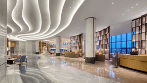 Un moderno vestíbulo de hotel con piso de mármol curvo, mostrador de recepción, zona de estar y amplias ventanas que ofrecen vistas.