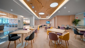 A modern dining area with wooden tables and colorful chairs, a patterned wall, and a ceiling with wooden slats and recessed lighting. - Holiday Inn Express Nanjing Happy Valley by IHG (Nanjing)