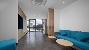 A modern waiting area with a blue sofa, a round wooden table, and a large window offering a view of the outdoors. - Holiday Inn Express Nanjing Happy Valley by IHG (Nanjing)
