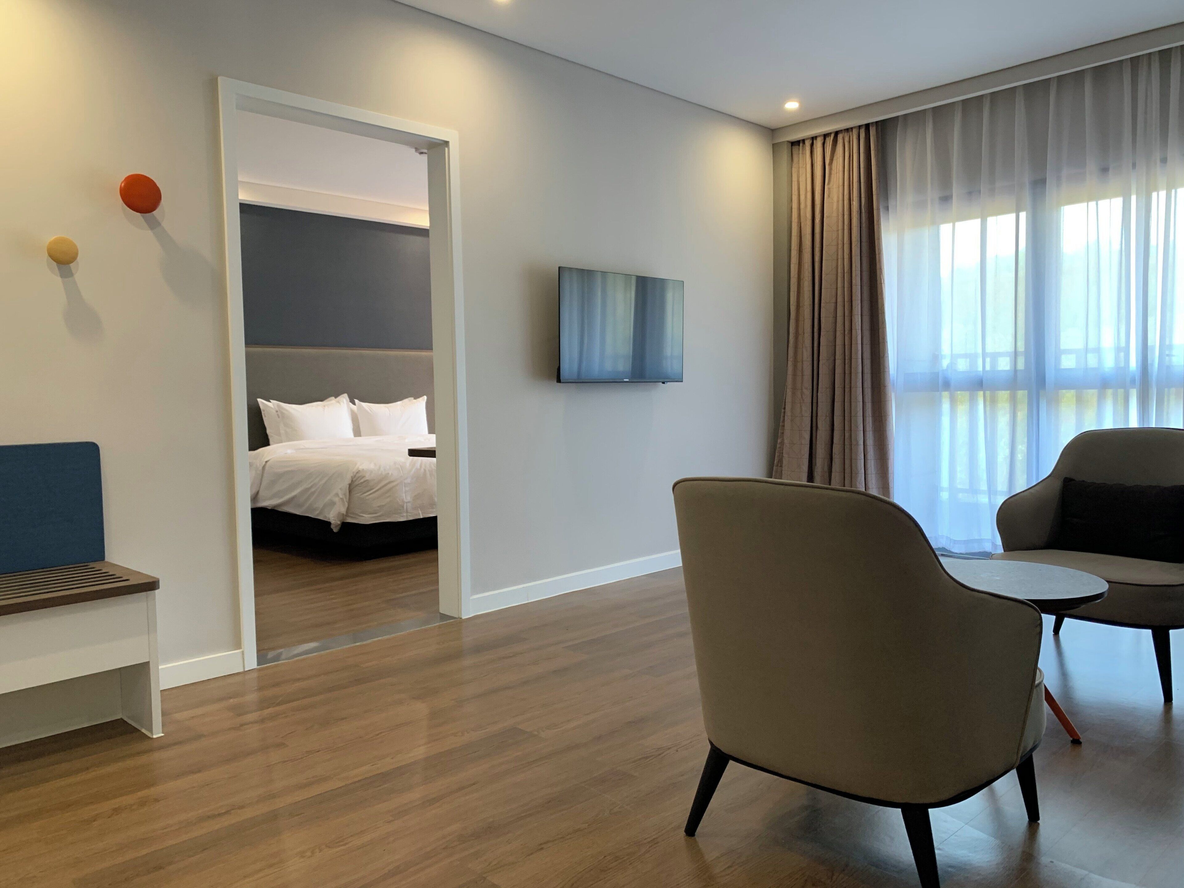 Habitació d'hotel amb un llit, zona de seients amb cadires, televisió i finestra amb cortines.