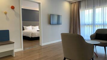 Habitació d'hotel amb un llit, zona de seients amb cadires, televisió i finestra amb cortines.