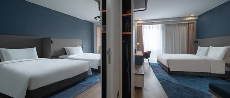 A hotel room with two beds, a desk, and a view of the outdoors.