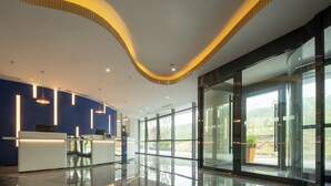 A modern reception area with a curved ceiling, glass doors leading to a view of greenery, and a reception desk with computers. - Holiday Inn Express Nanjing Happy Valley by IHG (Nanjing)
