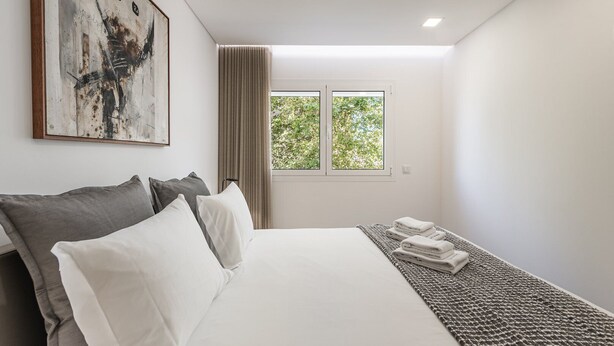 A modern hotel room with a large bed, a view of trees through the window, and a painting on the wall. - GuestReady - Tigerlily (Porto)