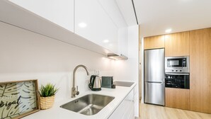 A modern kitchen with a stainless steel sink, a kettle, and a built-in microwave. - GuestReady - Tigerlily (Porto)