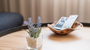 A small square glass vase with lavender on a wooden table, next to a remote control in a wooden bowl. - GuestReady - Tigerlily (Porto)