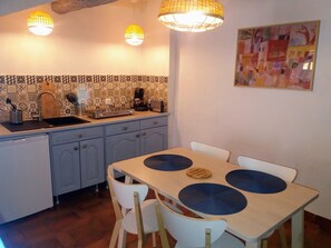 Une cuisine avec un plan de travail recouvert de carreaux, un évier, une machine à café et une table à manger avec des chaises.
