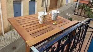 Een houten tafel met twee mokken en een lepel, een klein groen voorwerp, en een metalen bord met tekst.