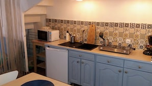 Een kleine keuken met een magnetron, spoelbak en fornuis, met een betegelde spatwand en blauwe keukenkastjes.