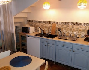 Een kleine keuken met een magnetron, spoelbak en fornuis, met een betegelde spatwand en blauwe keukenkastjes.