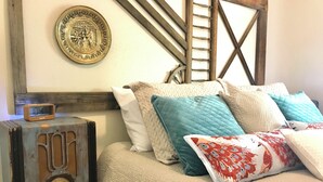 A bed with a quilted white cover, multiple pillows in various colors, a vintage radio, and a decorative plate on the wall. - Charming Centennial Cottage-Downtown! (Rapid City)