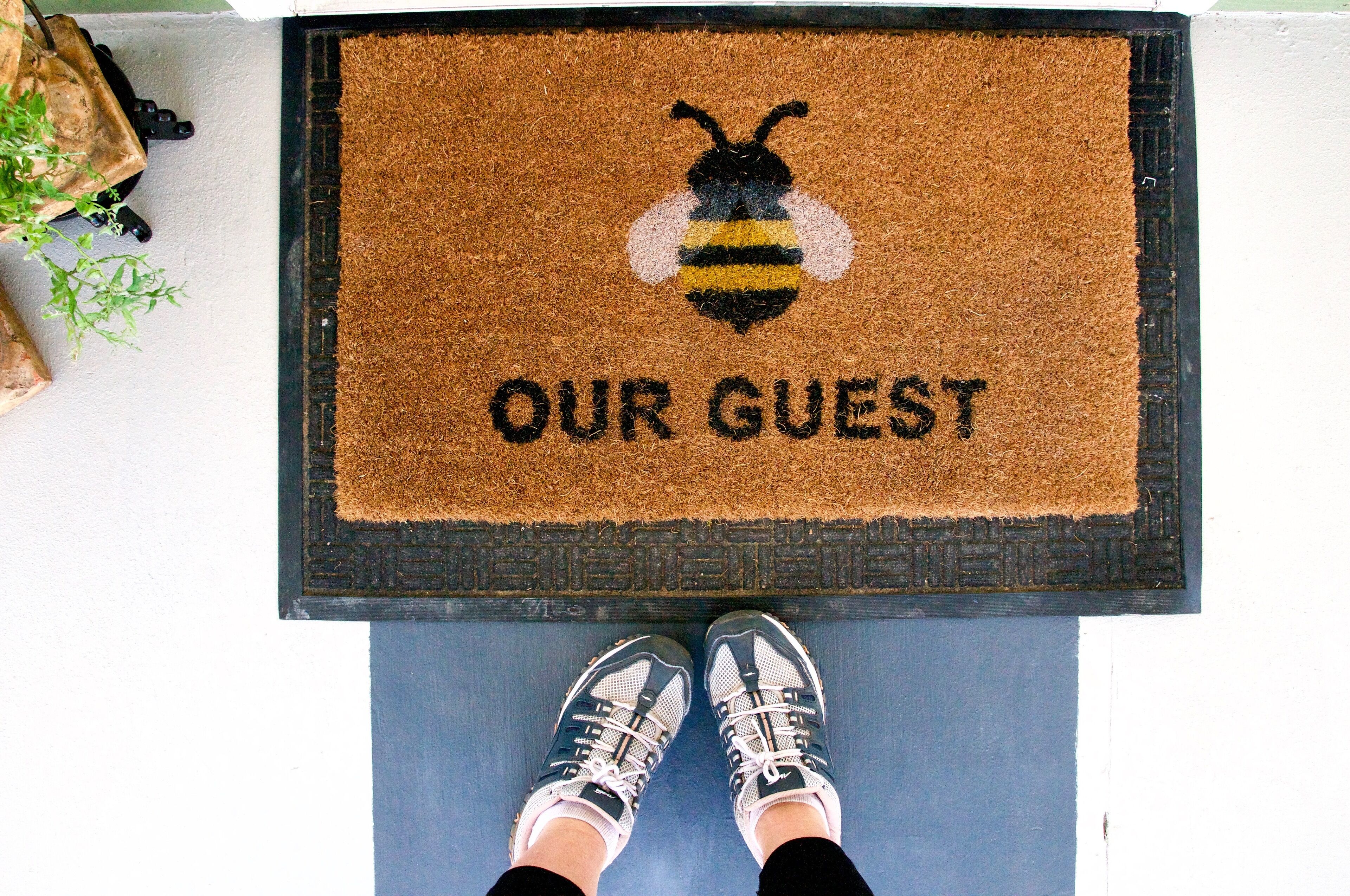 A doormat with a bee design and the words "OUR GUEST" on a blue floor.