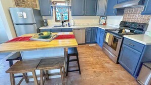 A kitchen with a wooden table, stools, a refrigerator, a stove, and blue cabinets. - Charming Centennial Cottage-Downtown! (Rapid City)