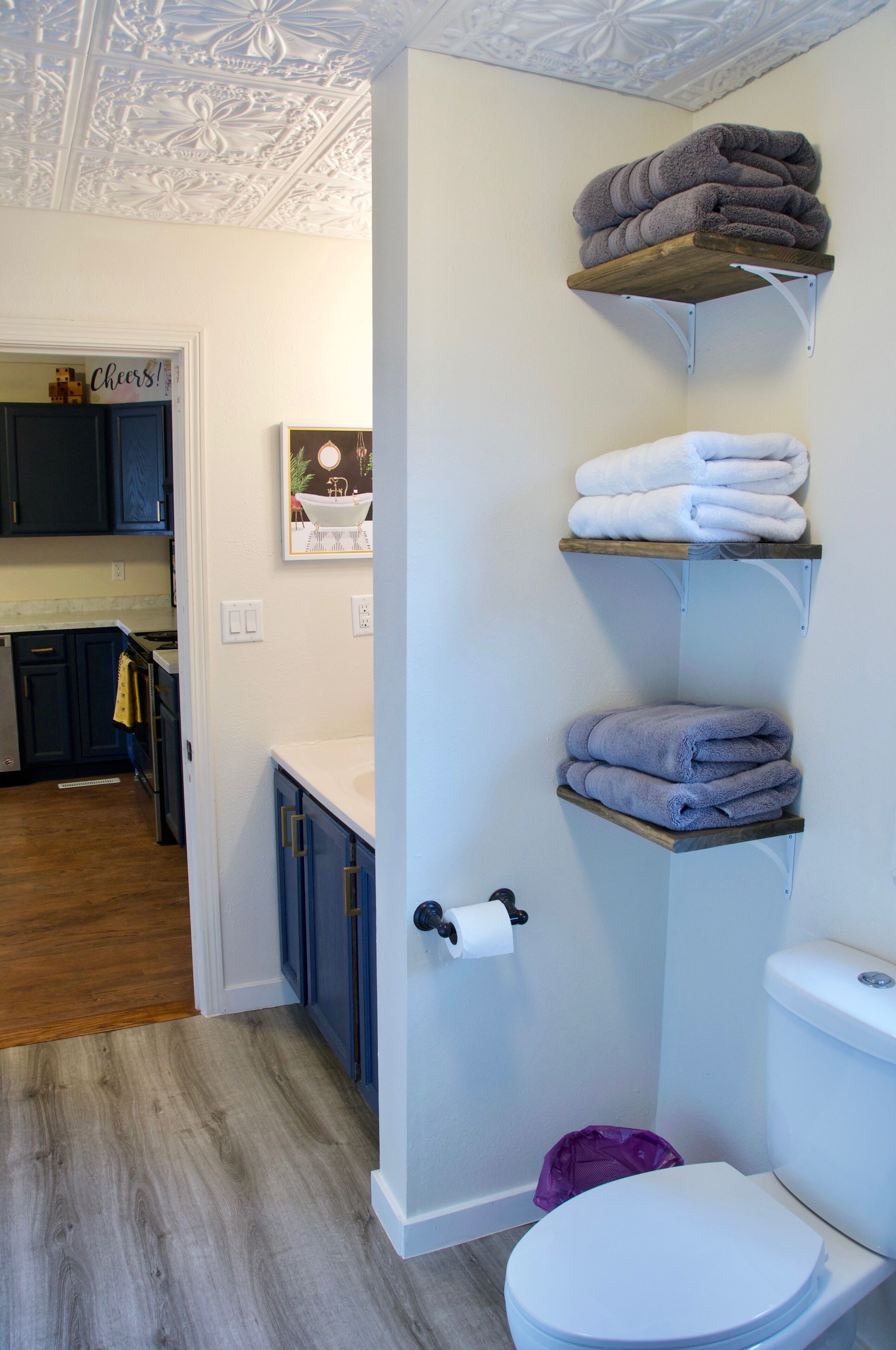 A bathroom with a toilet, a sink, and a shower. There are towels on shelves above the toilet.