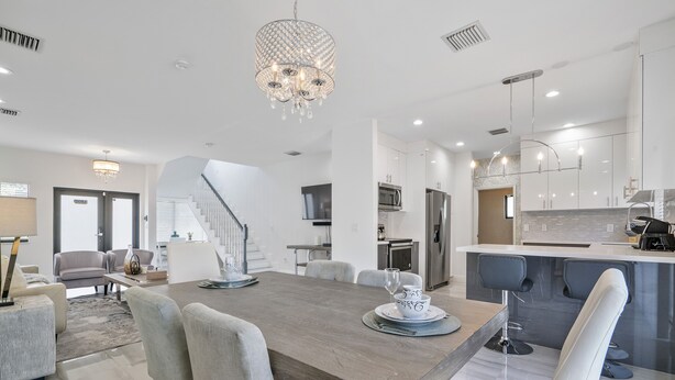 A spacious living area with a wooden dining table, modern kitchen, and a staircase leading to another level. - New Townhome near Wilton Manors/Las Olas (Fort Lauderdale)