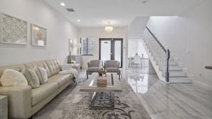 A spacious living room with a beige sofa, two armchairs, a coffee table, and a staircase leading to another level. - New Townhome near Wilton Manors/Las Olas (Fort Lauderdale)