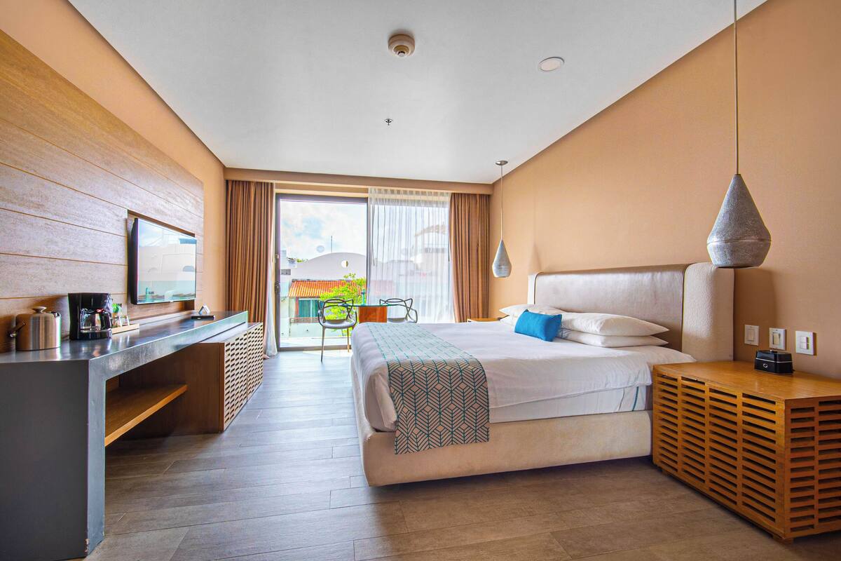 A modern hotel room with a bed, a desk, a chair, and a view of the outside.