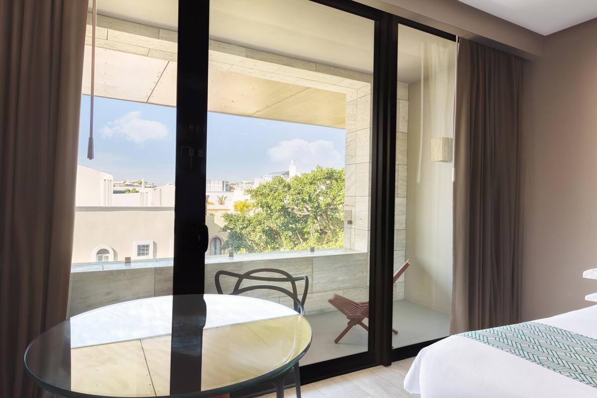 A hotel room with a balcony, a bed, a table, and a chair.