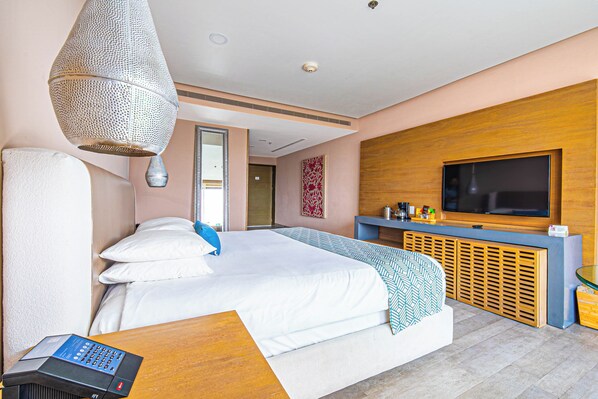 A modern hotel room with a large bed, a TV, a desk, and a hanging light fixture.