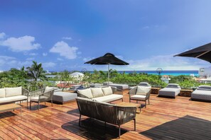 A wooden deck with outdoor seating, including sofas and chairs, overlooking a beach. - The Yucatan Playa del Carmen, Tapestry Collection by Hilton (Playa del Carmen)