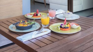 Uma mesa de jantar com itens de café da manhã, um sofá e uma televisão num quarto moderno com janelas grandes.
