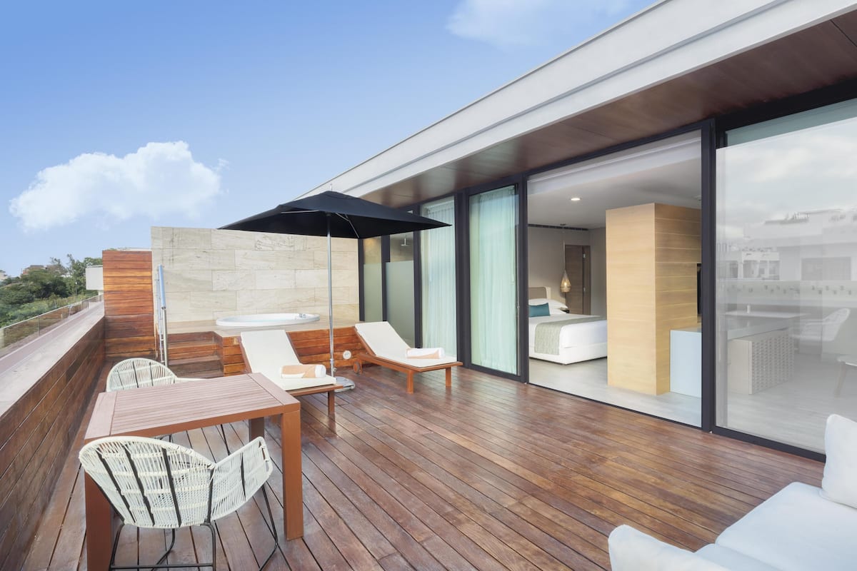 A modern outdoor patio with wooden flooring, white wicker chairs, a table, and a black umbrella.