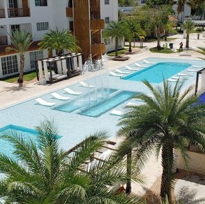 A pool area with two swimming pools, surrounded by palm trees and a building with balconies.