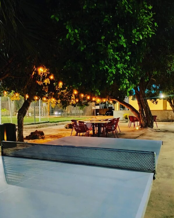 An outdoor dining area with a table and chairs, surrounded by trees and string lights.